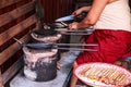 Woman baking Thong Muan Thai Crispy Coconut Wafer Rolls snack similar to pirouline in hot mold pans on charcoal earthen stoves.