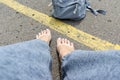 Woman with bare feet and backpack sitting on an asphalt road with a yellow single road line waiting vehicle for Royalty Free Stock Photo