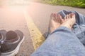 Woman with bare feet and backpack sitting on an asphalt road with a yellow single road line waiting vehicle for Royalty Free Stock Photo