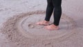 Woman with bare feet drawing smiley on sand near sea