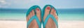 Woman bare sandy feet with blue flip flops, beach in the background Royalty Free Stock Photo