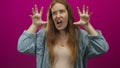 Woman with bared teeth snarling with raised hands in pink studio; anger defiance intensity ferocity Royalty Free Stock Photo