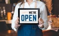 Woman barista wear jean apron holding come in we are open sign on tablet to customer at bar counter with smile emotion,Cafe Royalty Free Stock Photo