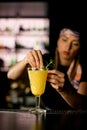 Woman bartender puts a sprig of rosemary while decorating glass with Blood orange paloma cocktail at the bar