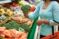 Woman with basket buying broccoli at grocery store