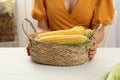 Woman with basket of corn cobs at white wooden table, closeup Royalty Free Stock Photo
