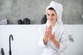 Woman in bath robe applying nourishing cream on hands after shower