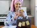 Woman in bath towel on her head and wearing bathrobe working with laptop and documents in kitchen at home, woman accountant Royalty Free Stock Photo