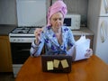 Woman in bath towel on her head and wearing bathrobe working with laptop and documents in kitchen at home, woman accountant Royalty Free Stock Photo