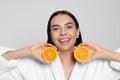 Woman in bathrobe holding juicy cut orange on light grey background. Spa treatment Royalty Free Stock Photo