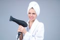 Woman in bathrobe and towel on head with hairdryer in studio. Portrait of female model with blow dryer. Hair care and Royalty Free Stock Photo