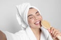 Woman in bathrobe with towel taking selfie while singing into brush on light grey background. Spa treatment Royalty Free Stock Photo