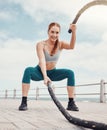 Woman, battle rope exercise and smile at ocean park for fitness, strong body and wellness at outdoor training. Girl