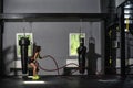 Woman with battle ropes exercise in the fitness gym. Young woman training in the dark gym