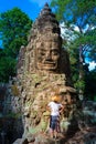 Woman in Bayon Temple looking at stone faces, Angkor Thom, morning light clear blue sky. Buddhism meditation concept, world famous