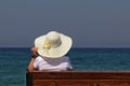 Woman in sun hat sitting on a wooden bench beach on blue sea background Royalty Free Stock Photo