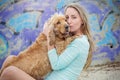 A woman on the beach with her Chocker Spaniel in front of a graffiti wall.