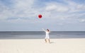 Woman on the beach throwing a red beach ball into the air