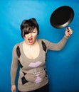 Woman beating with a frying pan on bluw studio background alone Royalty Free Stock Photo
