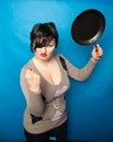 Woman beating with a frying pan on bluw studio background alone Royalty Free Stock Photo