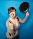 Woman beating with a frying pan on bluw studio background alone Royalty Free Stock Photo