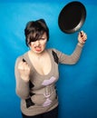 Woman beating with a frying pan on bluw studio background alone Royalty Free Stock Photo