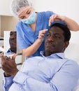 Woman beautician in mask examining face skin of afro american male patient Royalty Free Stock Photo