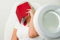 Woman beautician sits on a white armchair, tired, covered her face with a red notebook. Work seven days a week Royalty Free Stock Photo