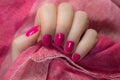 Woman with beautiful manicured pink fingernails gracefully crossing her hands to display them to the viewer on a pink background Royalty Free Stock Photo