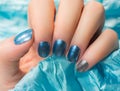 Woman with beautiful nail blue fingernails gracefully crossing her hands to display them to the viewer on a silver background in a Royalty Free Stock Photo