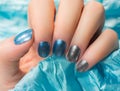 Woman with beautiful nail blue fingernails gracefully crossing her hands to display them to the viewer on a silver background in a Royalty Free Stock Photo