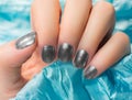Woman with beautiful nail blue fingernails gracefully crossing her hands to display them to the viewer on a silver background in a Royalty Free Stock Photo