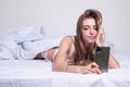 Woman in bed checking social apps with smartphone. Sexy girl making video call, lying on bed in the morning.