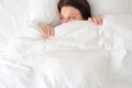 Woman in bed looking surprised from under blanket