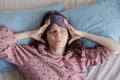woman in bed wakes up, insomnia and sleep disorder. person in sleep mask holds his head and face Royalty Free Stock Photo