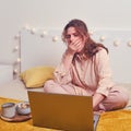 A woman on the bed yawns while sitting at her laptop. The girl works with food on the bed