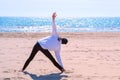 Woman beginner does triangle yoga pose sand sea beach sport exercise back view.