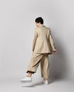 Woman in beige business casual pantsuit and sneakers dances, standing with one leg back. Stylish business female wear