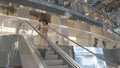 Woman in beige coat and black hat going down the escalator inside the modern shopping center. Action. Young female Royalty Free Stock Photo