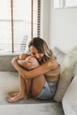 Woman in beige crop top and denim shorts sitting on a sofa bed and holding her knees