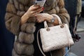 Woman with beige leather Christian Dior bag and brown fur coat looking at smartphone before fashion Albino