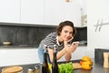 Woman bending on kitchen counter with smartphone, looking for healthy recipe online on mobile phone, standing next to