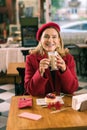 Beaming blonde-haired woman wearing red coat and beret drinking coffee