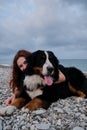 Woman and Bernese Mountain Dog are lying on the beach happy. Young red haired cute Caucasian girl is relaxing on beach with her Royalty Free Stock Photo