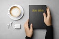 Woman with Bible, cup of coffee and earphones at grey table, top view. Religious audiobook