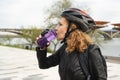 A woman in a bicycle helmet drinks water after cycling. Sportswoman drinks water from a bottle