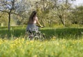 Woman on bicycle in a meadow with yellow flowers and trees in beautiful nature, driving away