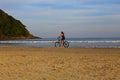 Woman riding her bicycle on the sand in front of the sea. Riviera beach, Bertioga, Brazil