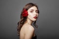 Woman with a big red flower in her hair. Brown-haired girl with a red flower posing on a gray background. Big beautiful eyes Royalty Free Stock Photo