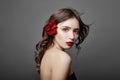 Woman with a big red flower in her hair. Brown-haired girl with a red flower posing on a gray background. Big beautiful eyes